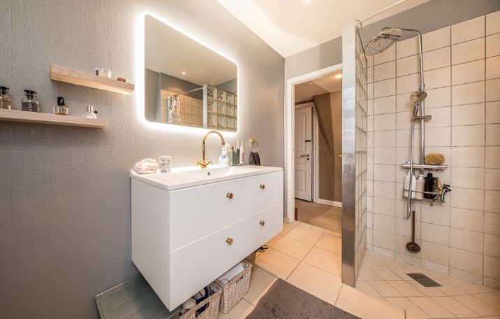 badeværelse med hvidt badeværelsesmøbel, bruseniche med hvide fliser og grå vægge. Spejl med lys