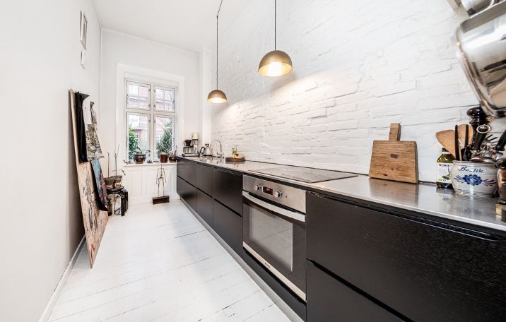 aflangt køkken med hvide lofter, gulve og vægge og sort køkken op ad den ene væg